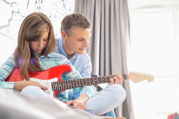 Father and daughter playing electric guitar at home